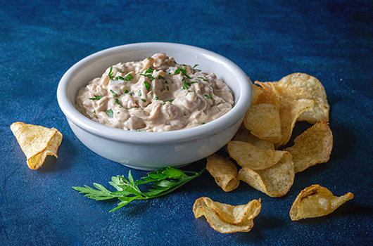 Vegan Caramelized Onion Dip in a white bowl with seasoned potato chips and a sprig of parsley