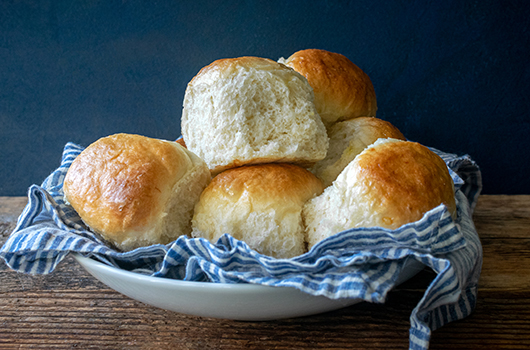 Mashed Potato Dinner Rolls resting on a blue cloth , on a white plate, on a wooden table