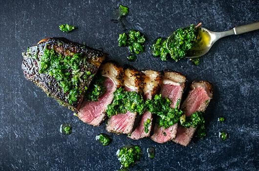 New York Steak slathered with green Chimichurri from a spoon.
