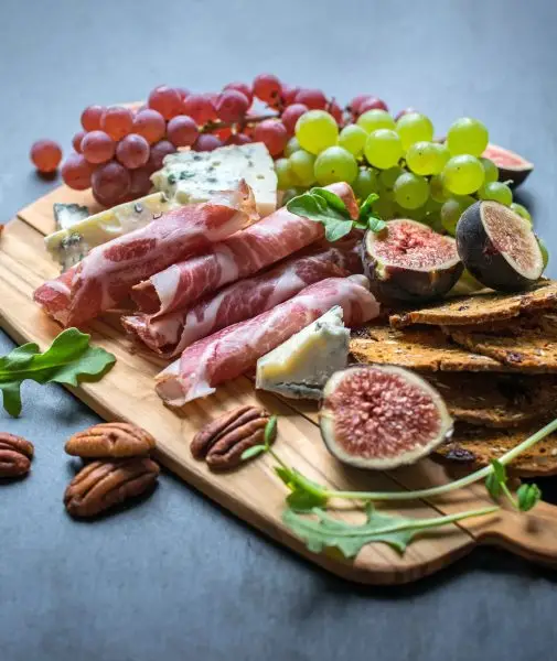 Charcuterie board with figs, crackers, pecans, blue cheese, red and green grapes, and capocollo