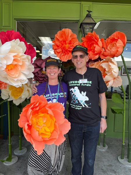 Marie and Alex pose in front of hand made paper flowers at LifeSource Food Fair, May 3rd 2025,