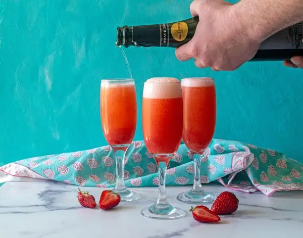 Strawberry vanilla bean bellinis, hand pouring sparkling wine into glasses
