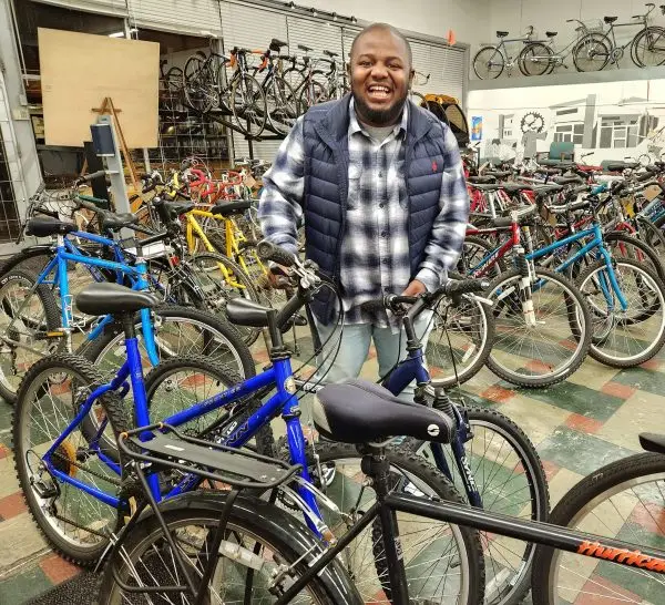 Man holding a bicycle inside The Northwest Hub nonprofit bike shop in Salem, Oregon, surrounded by refurbished bikes