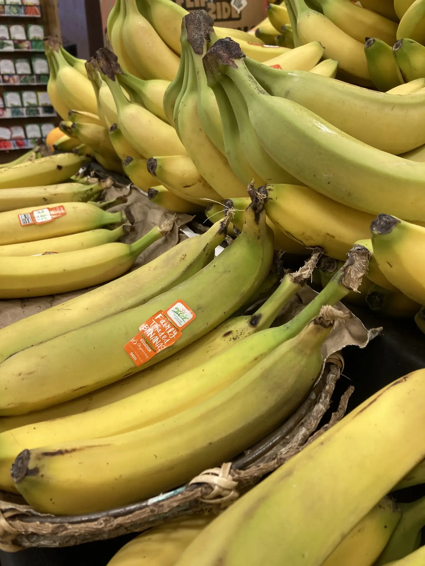 Close-up of organic GROW bananas stacked in a produce display, featuring Fair Trade banana labels and vibrant yellow and green fruit.