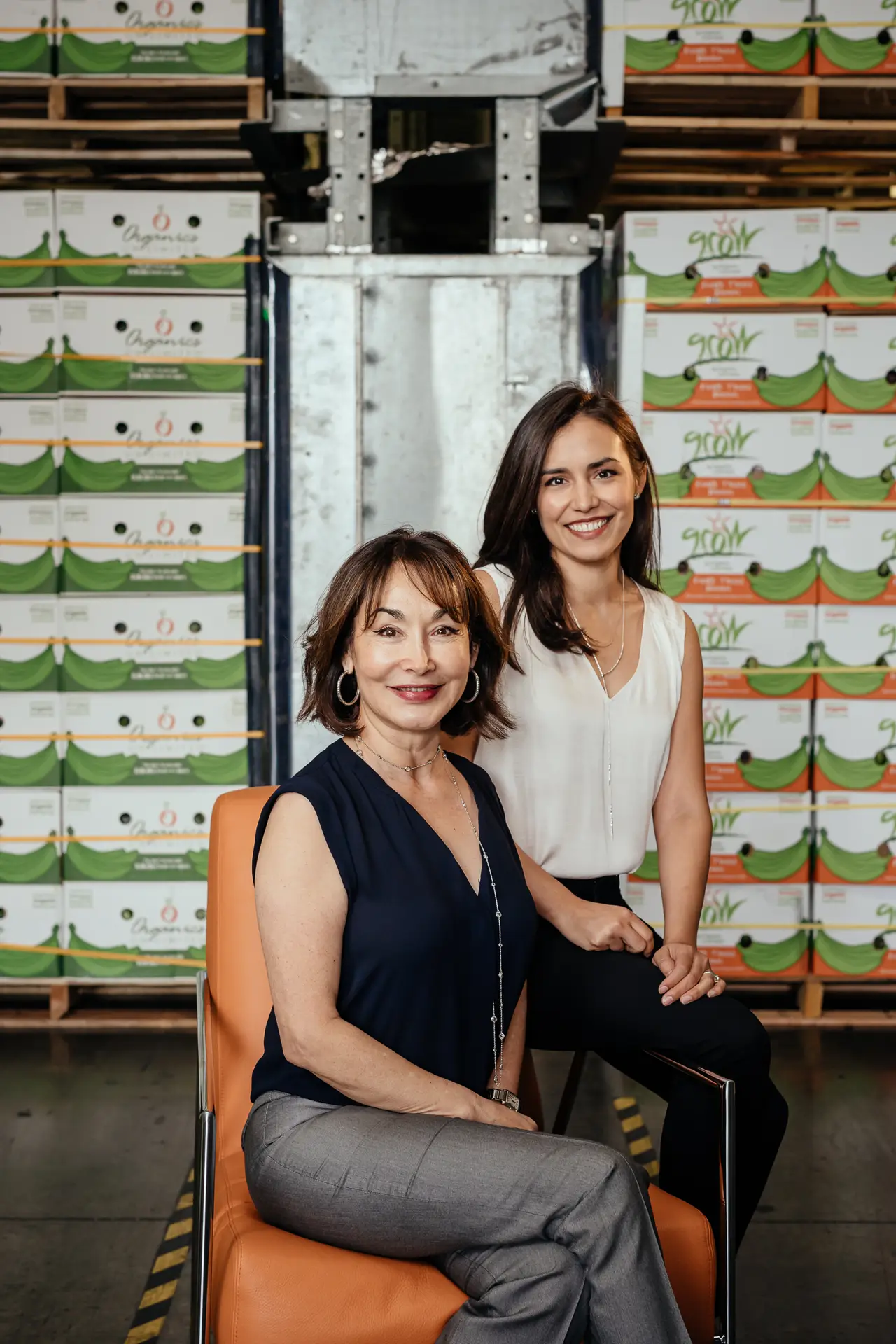 Mayra Velázquez de León and Daniella Velázquez de León of Organics Unlimited pose in a warehouse surrounded by boxes of GROW and Organics Unlimited bananas.