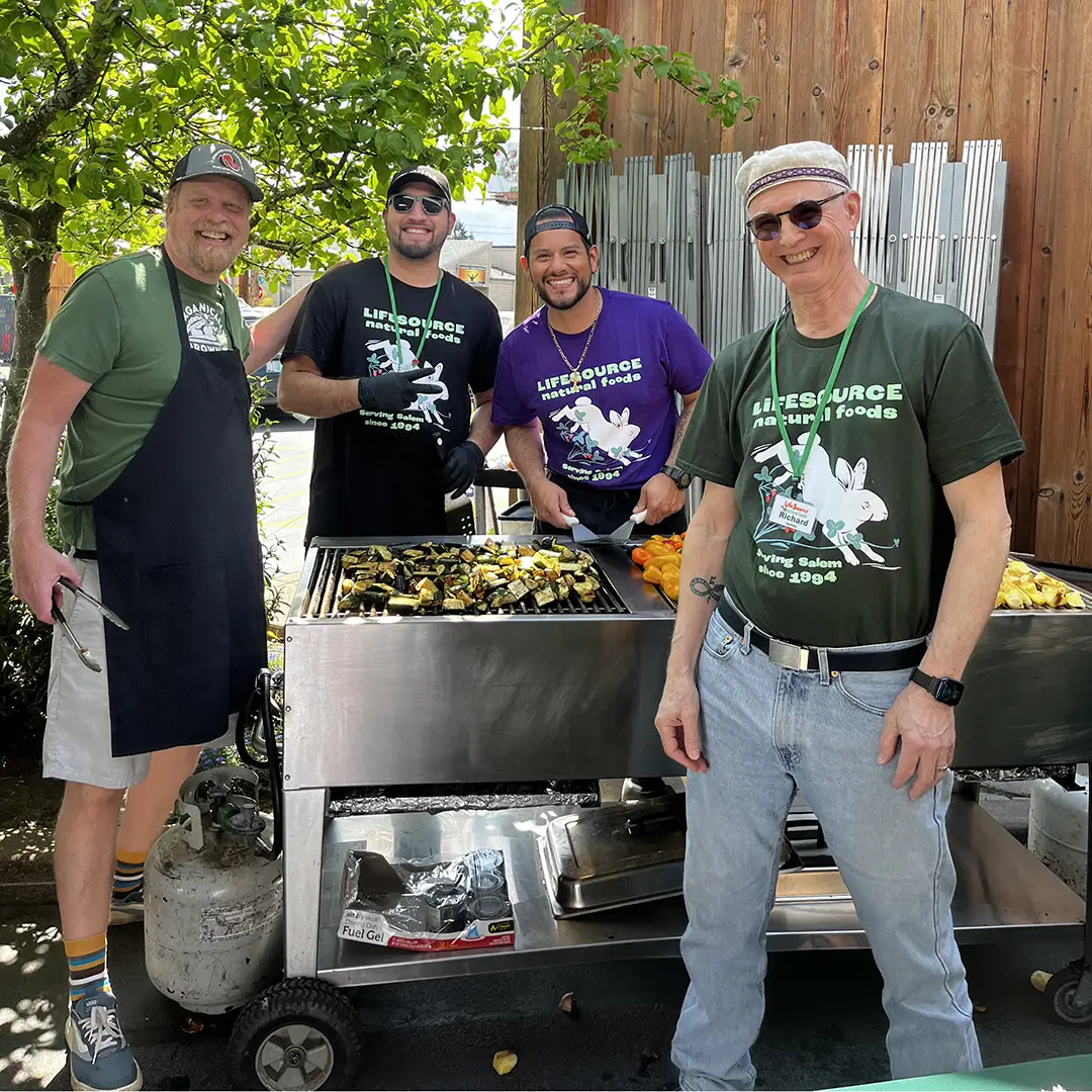 LifeSource team members smiling together while grilling fresh vegetables at the outdoor Food Fair veggie BBQ.