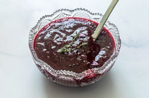 Deep red scratch-made cranberry sauce served in a glass bowl with fresh herb garnish.