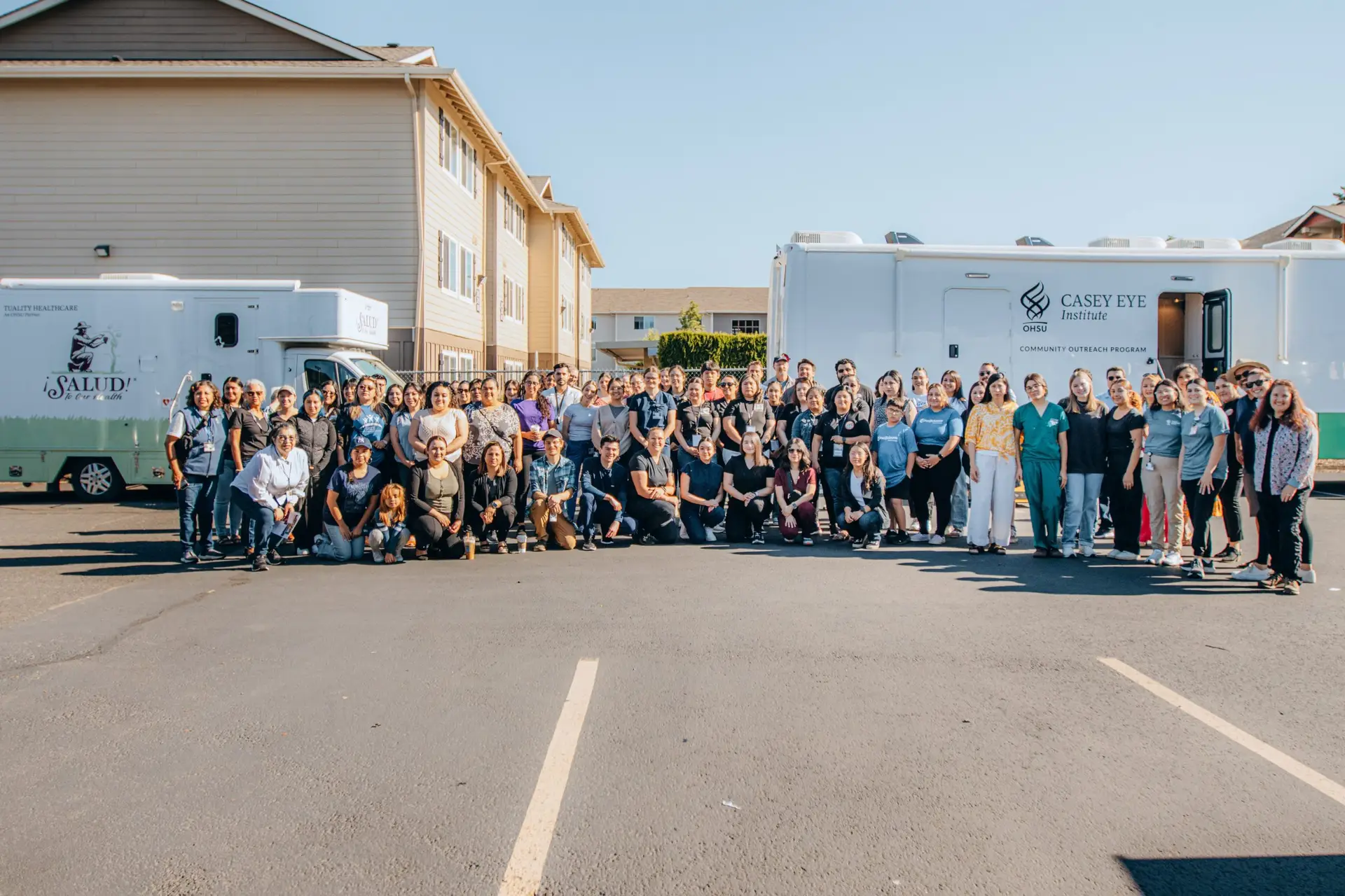 Mano a Mano Family Center community group gathers beside ¡Salud! and OHSU Casey Eye Institute mobile health clinics.