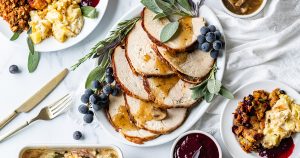 Sliced roasted turkey breast with mushroom gravy, surrounded by scratch-made holiday sides including stuffing, mac and cheese, cranberry sauce, potatoes, and green bean casserole.