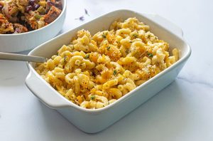 Creamy baked macaroni and cheese topped with herbs and toasted breadcrumbs in a white casserole dish.