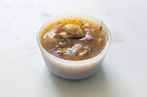 Bowl of savory mushroom gravy with sliced mushrooms and fresh herb garnish.