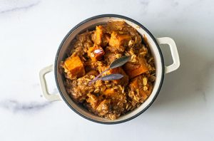 Sweet potato casserole with roasted sweet potato pieces and a savory walnut topping, garnished with fresh sage.