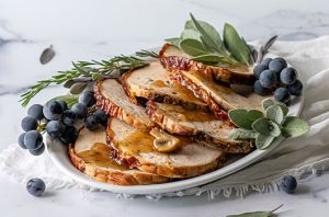 Sliced roasted turkey breast topped with mushroom gravy and garnished with fresh sage, rosemary, and grapes.