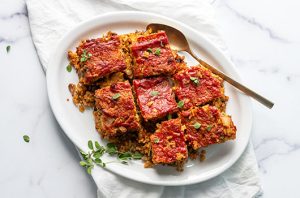 Sliced walnut loaf topped with savory tomato glaze and fresh herbs on a white serving platter.